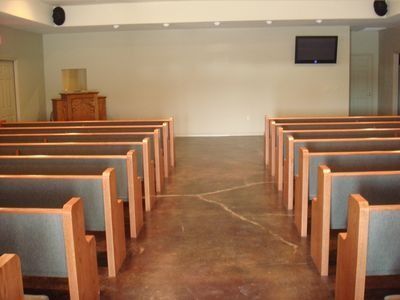 Empty church sanctuary with rows of wooden pews facing a pulpit and wall-mounted screen