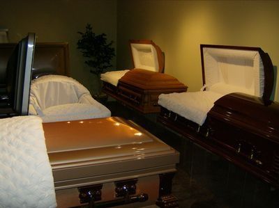 Four polished wooden caskets with white linings displayed in a funeral showroom