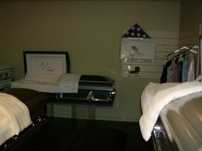 Dark room with two beds and a wall-mounted TV, resembling a hotel room or showroom