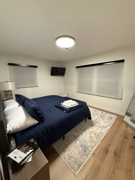Bedroom with bed, dark wall, windows with shades, nightstands, and artwork.