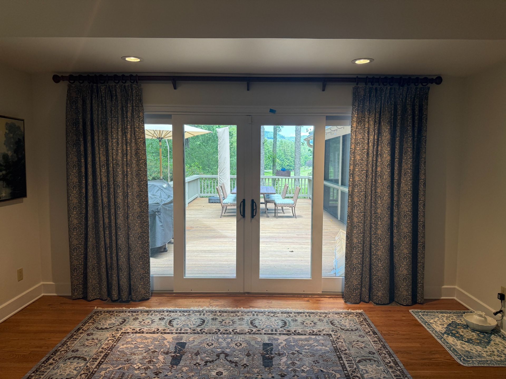 Living room with large glass doors, blue curtains, wood floor, and a patterned rug opening to a patio.