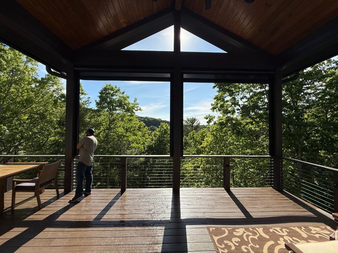 Covered wooden deck overlooking trees, with a person standing by the railing.