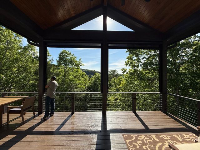 Covered wooden deck overlooking trees, with a person standing by the railing.