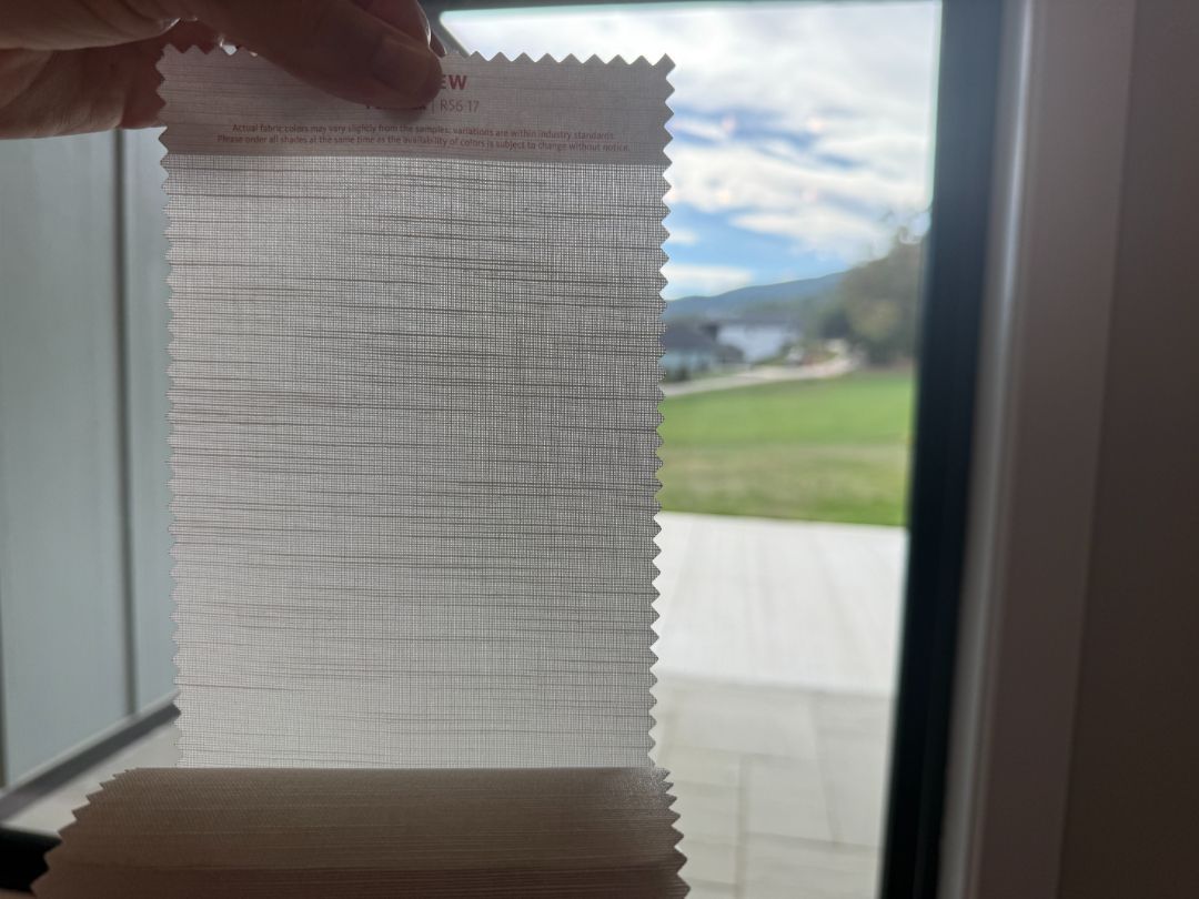 Hand holding a small window blind sample with a bright outdoor view in the background