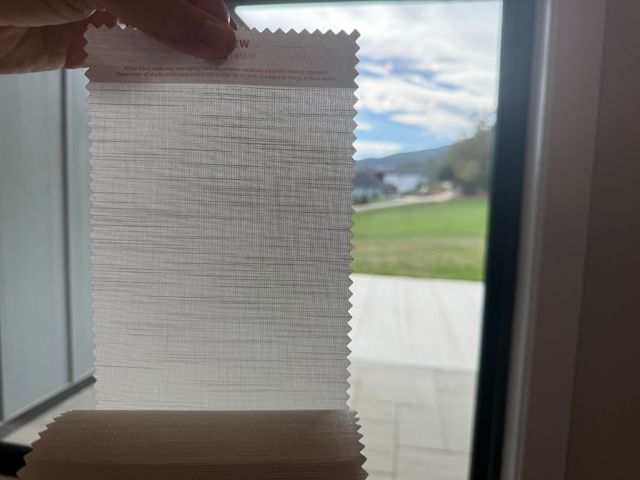 Hand holding a small window blind sample with a bright outdoor view in the background
