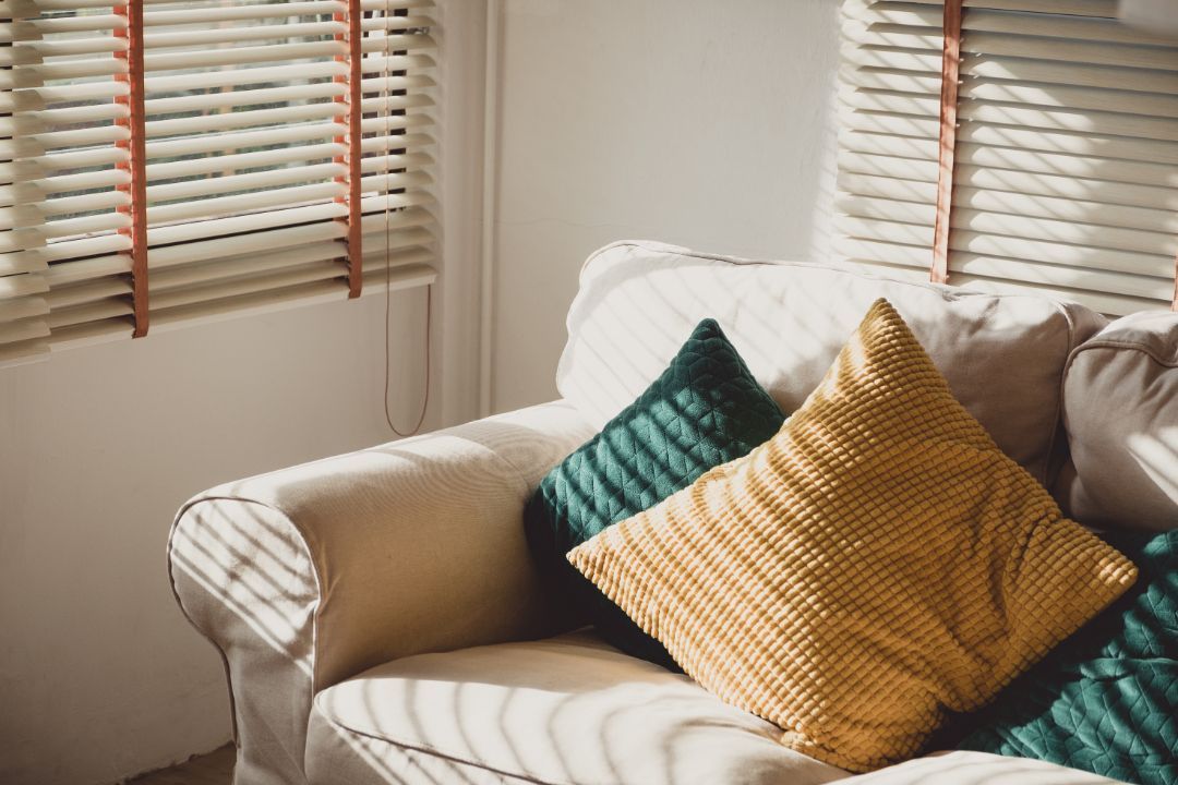 Sunlit sofa by window with striped blinds and teal and mustard pillows