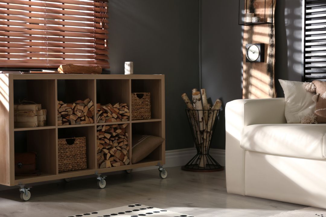 Sunlit living room with white sofa, wood cube shelf, woven blinds, and a vase of branches.