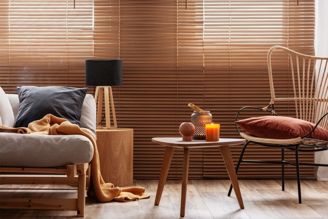 Cozy living room with dog on chair, warm lamp, side table, woven chair, and wooden blinds