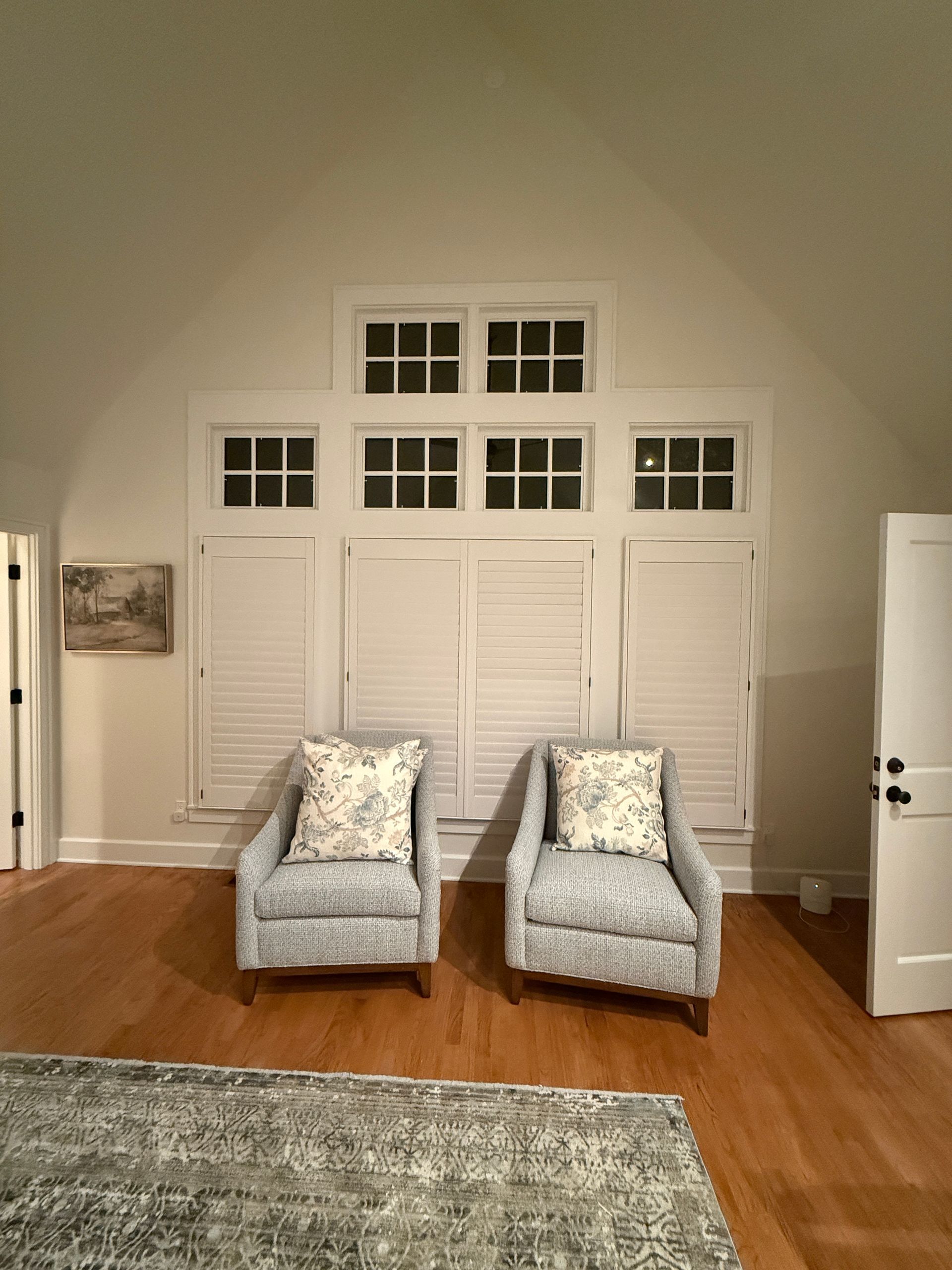 Cozy living room with two gray armchairs, hardwood floors, and a white wall of windows and shutters
