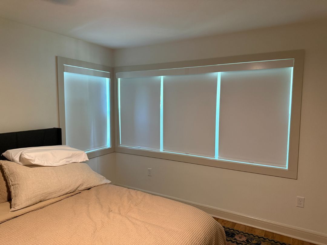 Bedroom corner with a bed and two large windows with white blinds and beige walls