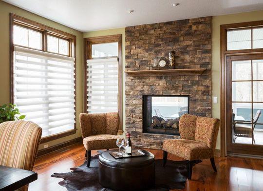 Cozy living room with stone fireplace, wicker chairs, large windows, and a view of the water.
