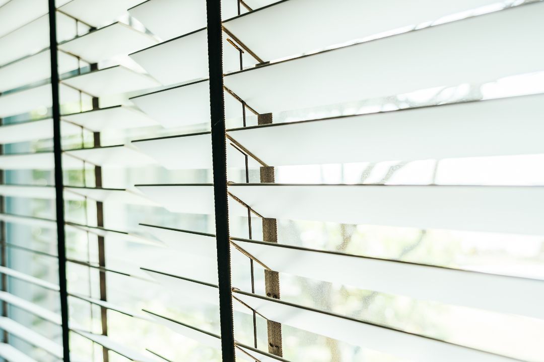 White window blinds with light filtering through slats, viewed close up.