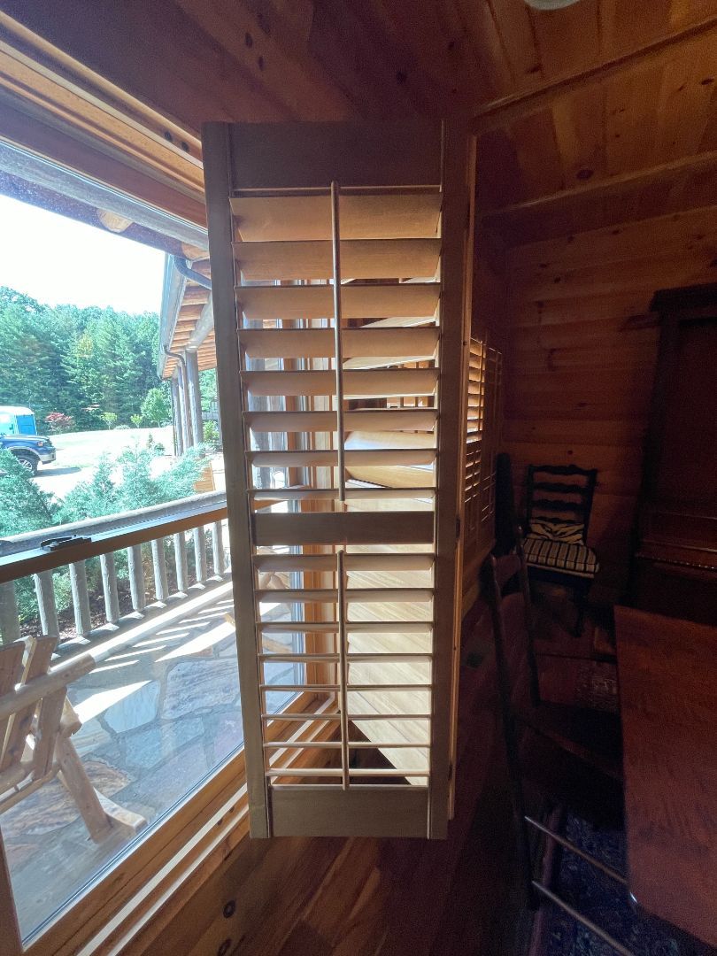 Wooden porch with open shutter door, railings, and a sunlit outdoor view through a window