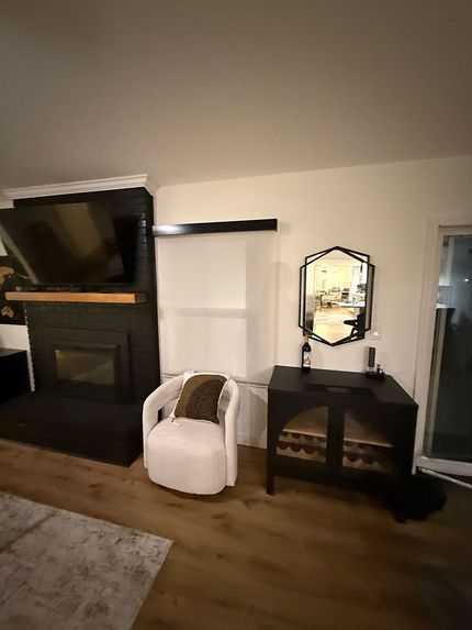 Living room with a large TV above a fireplace, seating area, and outdoor view.