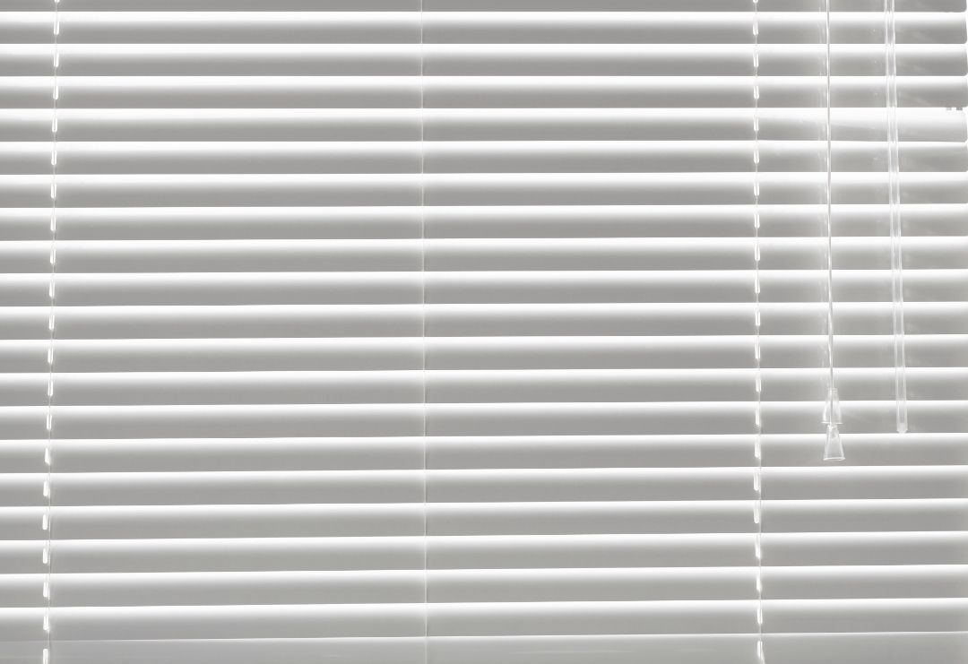 White window blinds with a pull cord, partially closed.