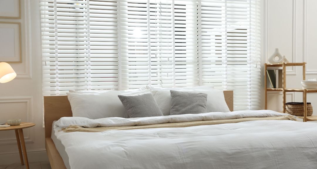 Cozy bedroom with a white bed, gray pillows, and sunlit shutters behind it