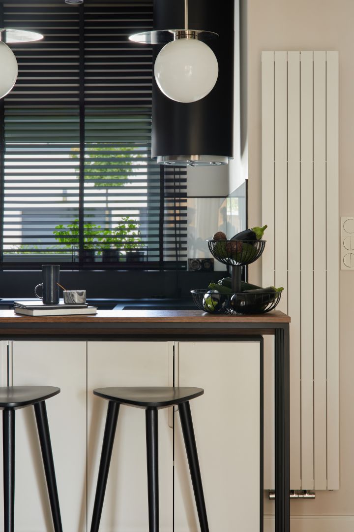 Modern kitchen with black blinds, white pendant lights, and two stools at a counter.