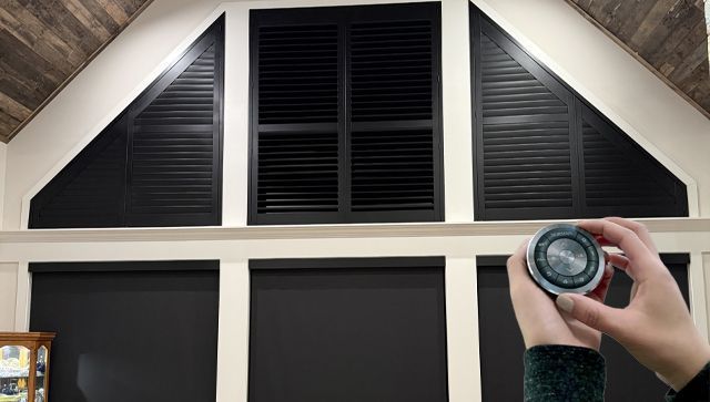 Hand holding a round flashlight near a vaulted window with dark shutters and white trim