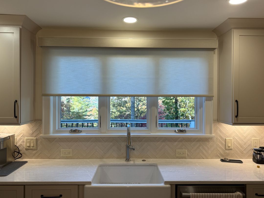 Bright kitchen with a large window, white counters, and a sink beneath a closed blind.