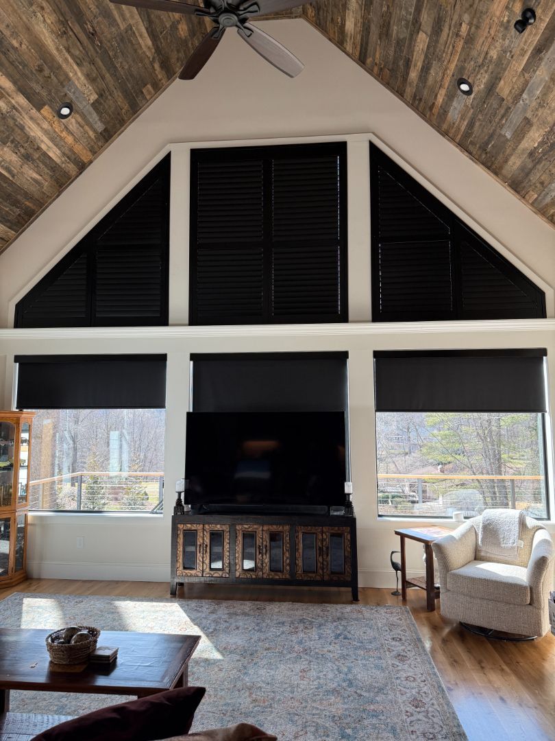 Modern living room with vaulted ceiling, black shutters, fireplace, and white armchairs by large windows