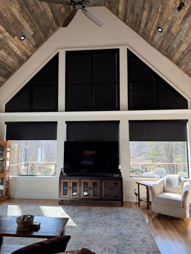 Modern living room with vaulted ceiling, black shutters, fireplace, and white armchairs by large windows