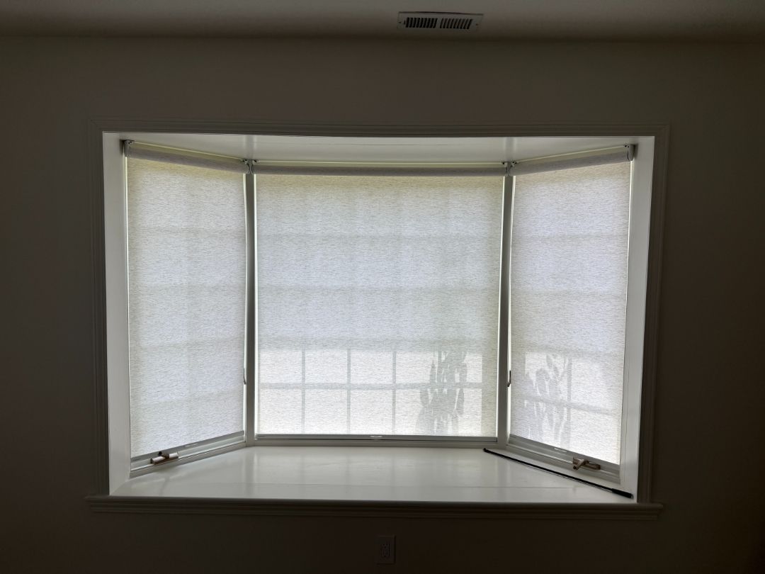 Empty bay window with white blinds and a built-in bench seat in a dim room