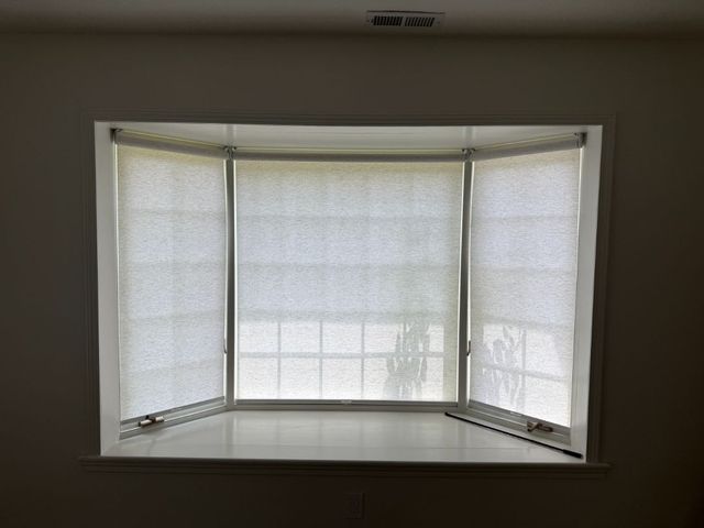 Empty bay window with white blinds and a built-in bench seat in a dim room