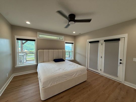 Bright bedroom with white bed, beige walls, ceiling fan, and French closet doors