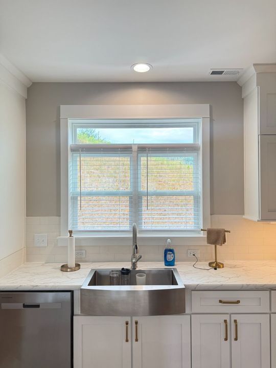 Modern kitchen sink under a window with white cabinets and a stainless dishwasher