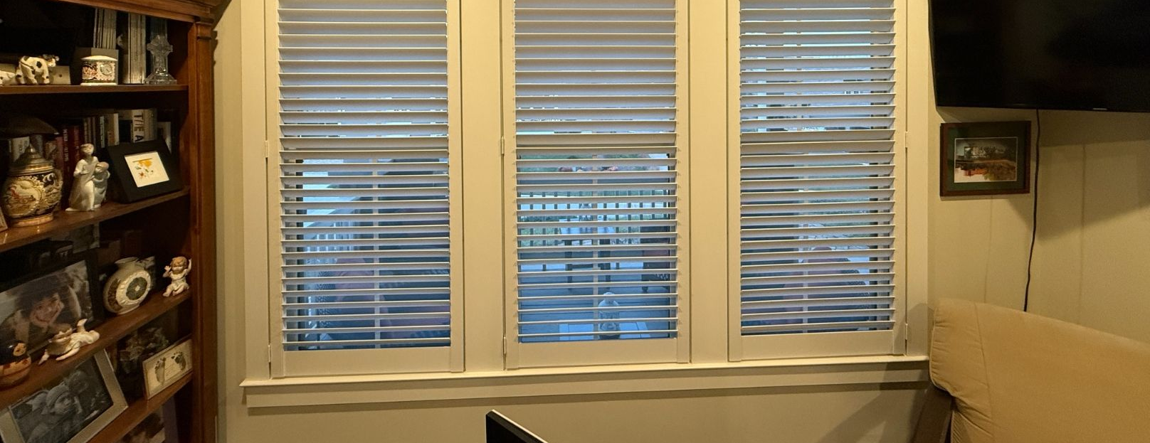 Living room window with white blinds and built-in shelves displaying decor on the left