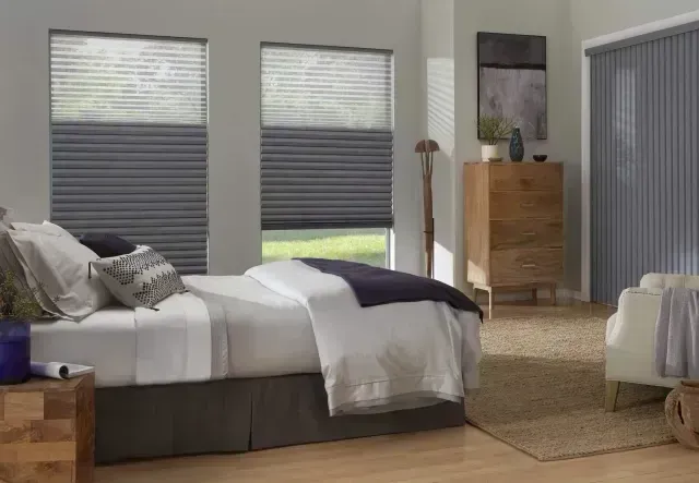 Bedroom with bed, windows, chest of drawers, and armchair; soft neutral tones and light.