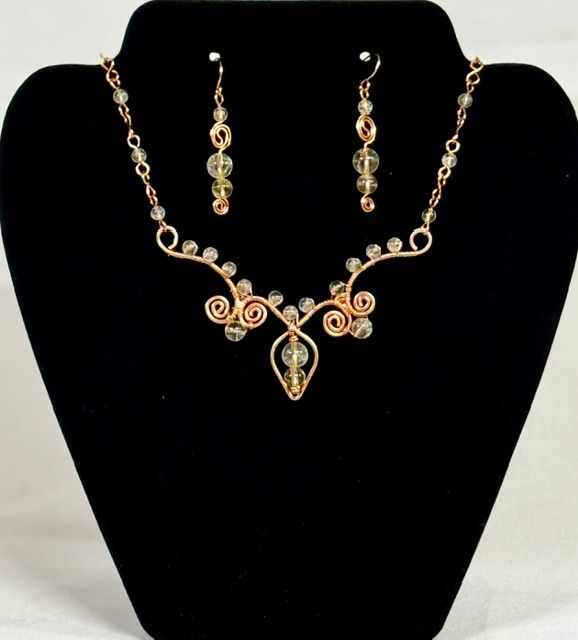 Gold necklace and matching earrings with gemstones displayed on a black jewelry bust.