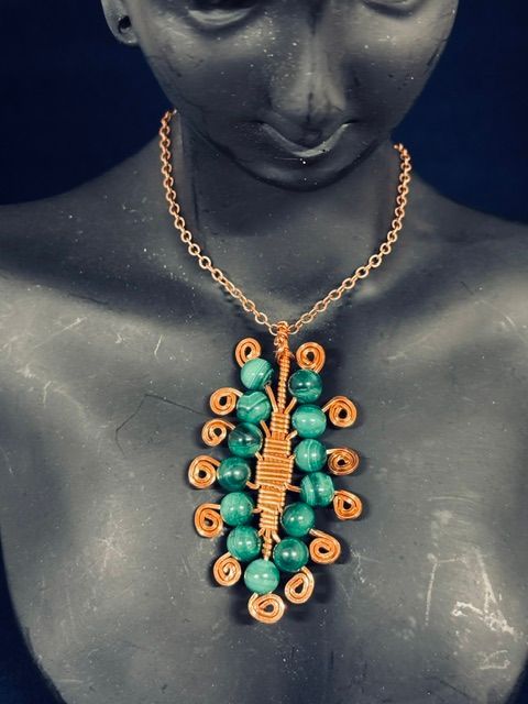 Black mannequin wearing a gold chain necklace with green and tan beaded pendant details