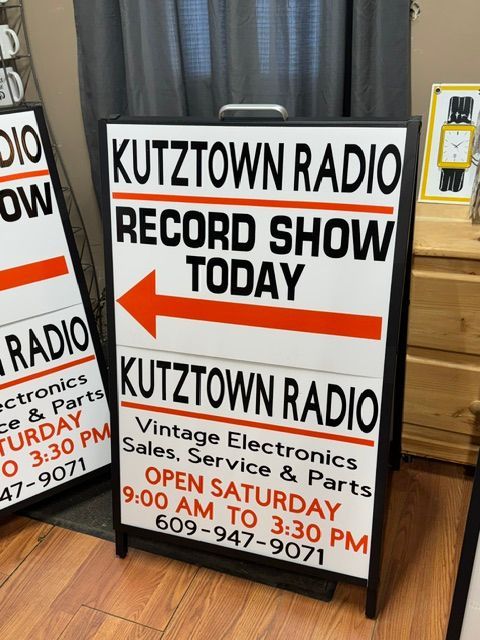 A-frame sign for Kutztown Radio Record Show Today, orange arrow pointing left, in storefront window.