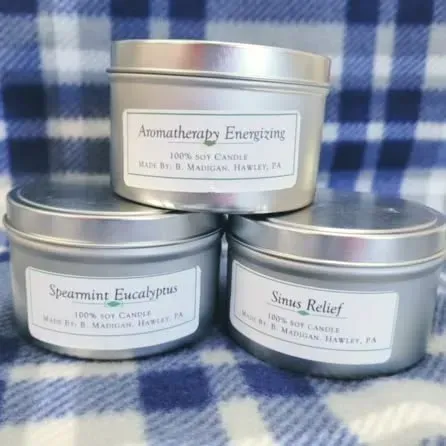 Three silver tins of scented candles on a blue plaid blanket