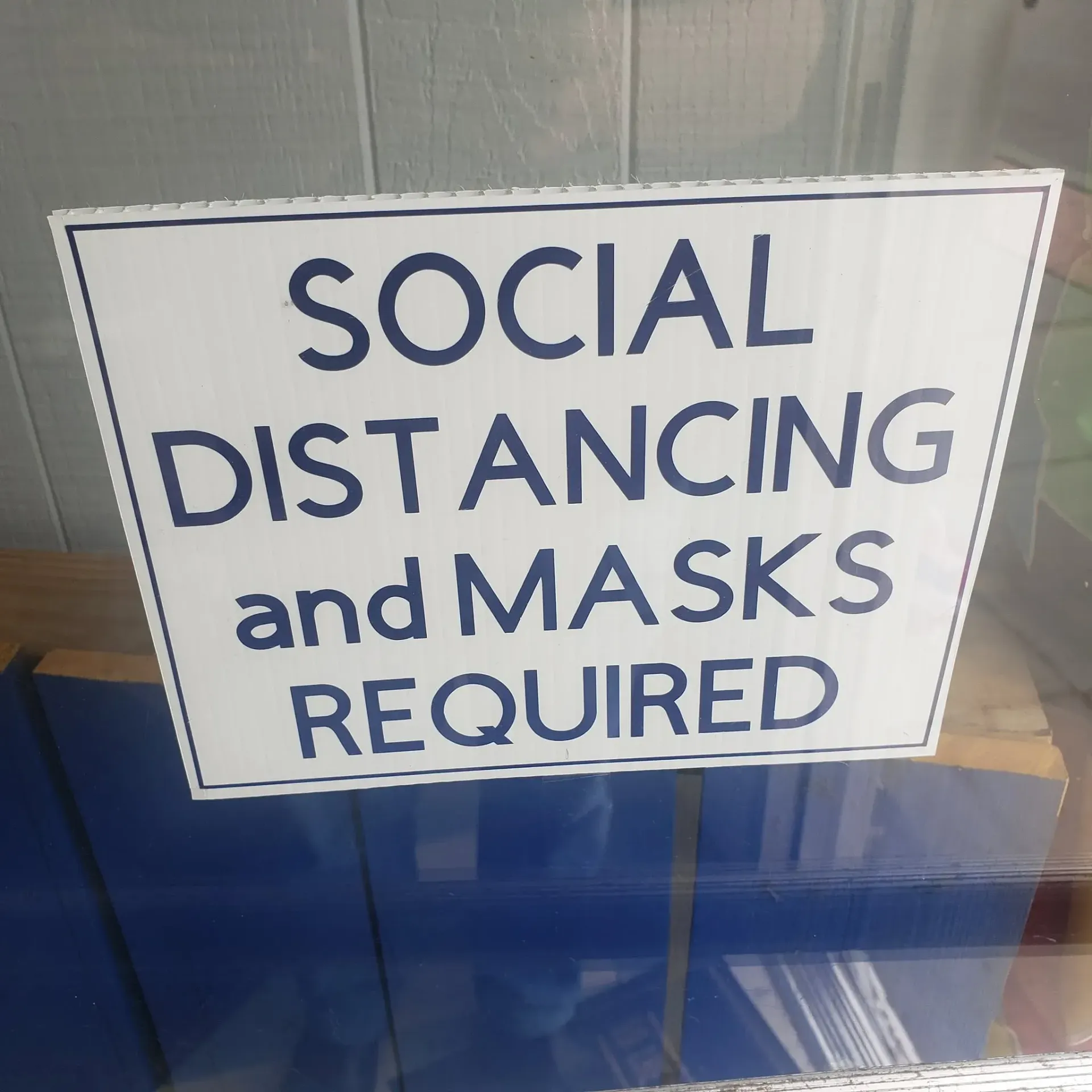 Sign reading “Social distancing and masks required” in blue text on a white background