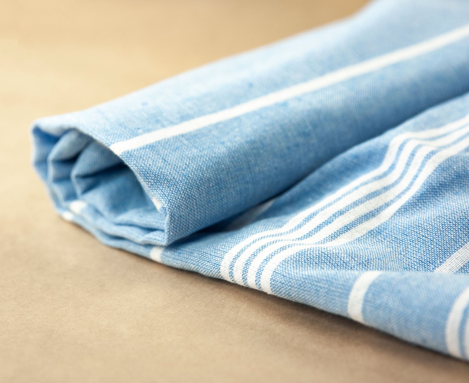 Folded light blue striped cloth on a tan surface
