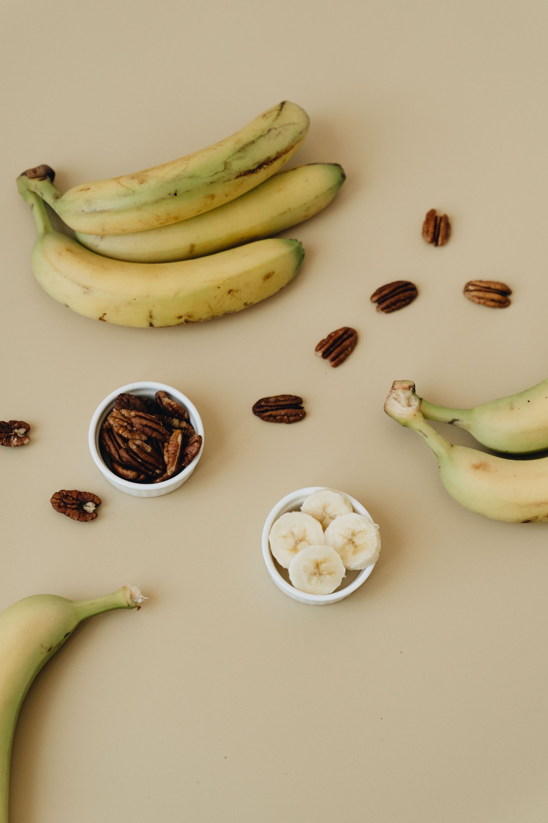 Bananas, dates, and sliced banana in small bowls on a beige background