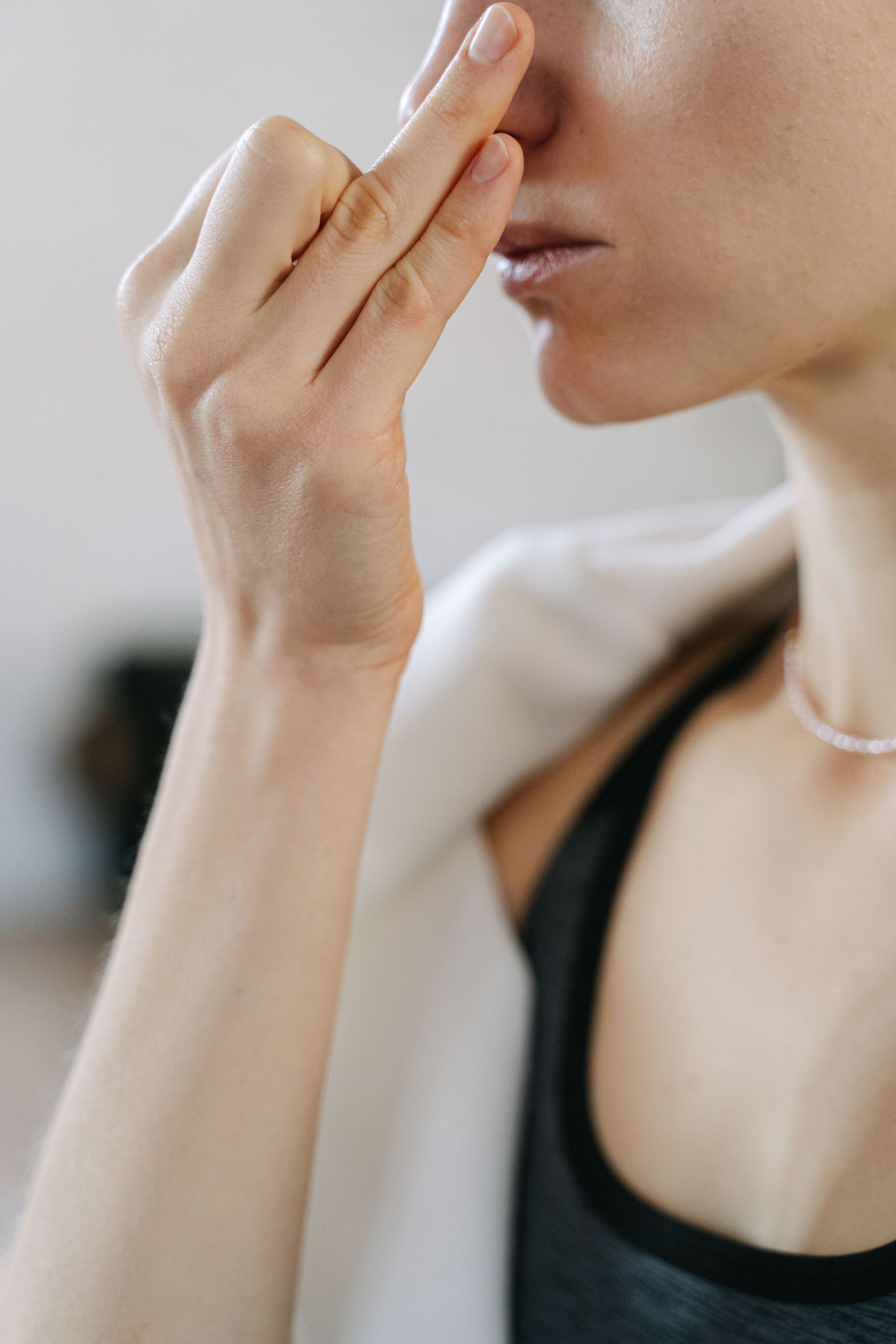Woman pinching her nose, wearing a black top and white shawl