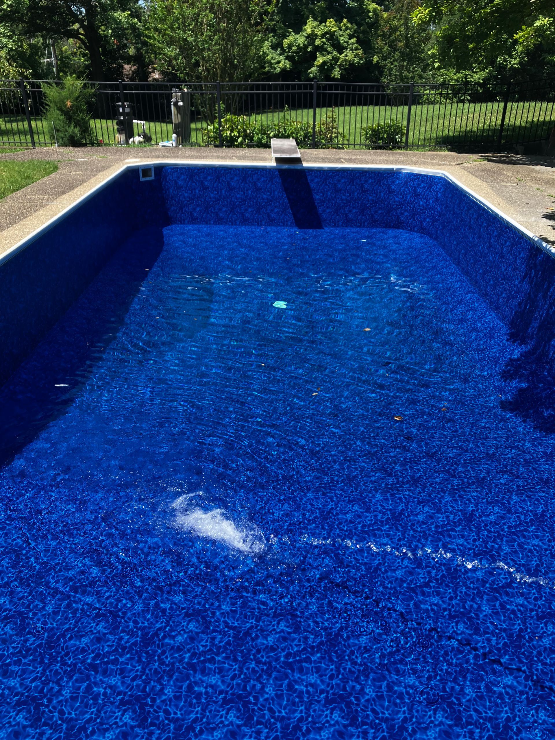 Blue swimming pool with rippling water and a deck railing in the background