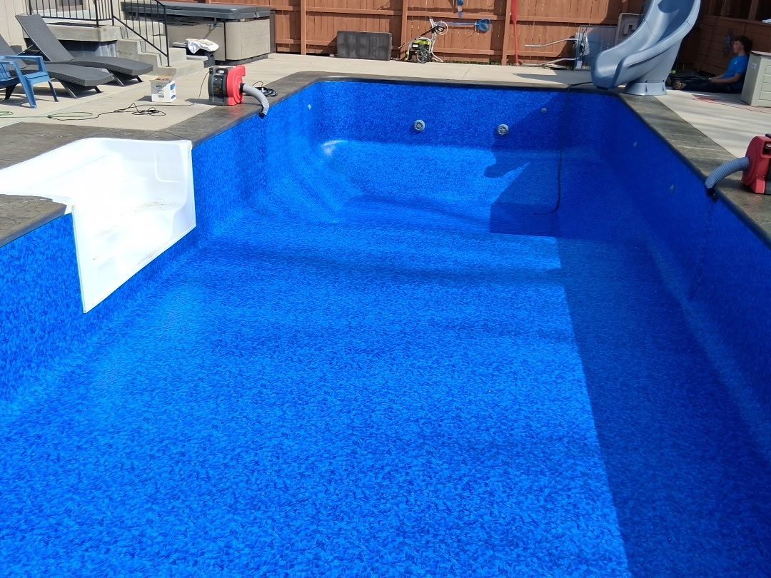Bright blue swimming pool under construction with white walls and construction materials nearby