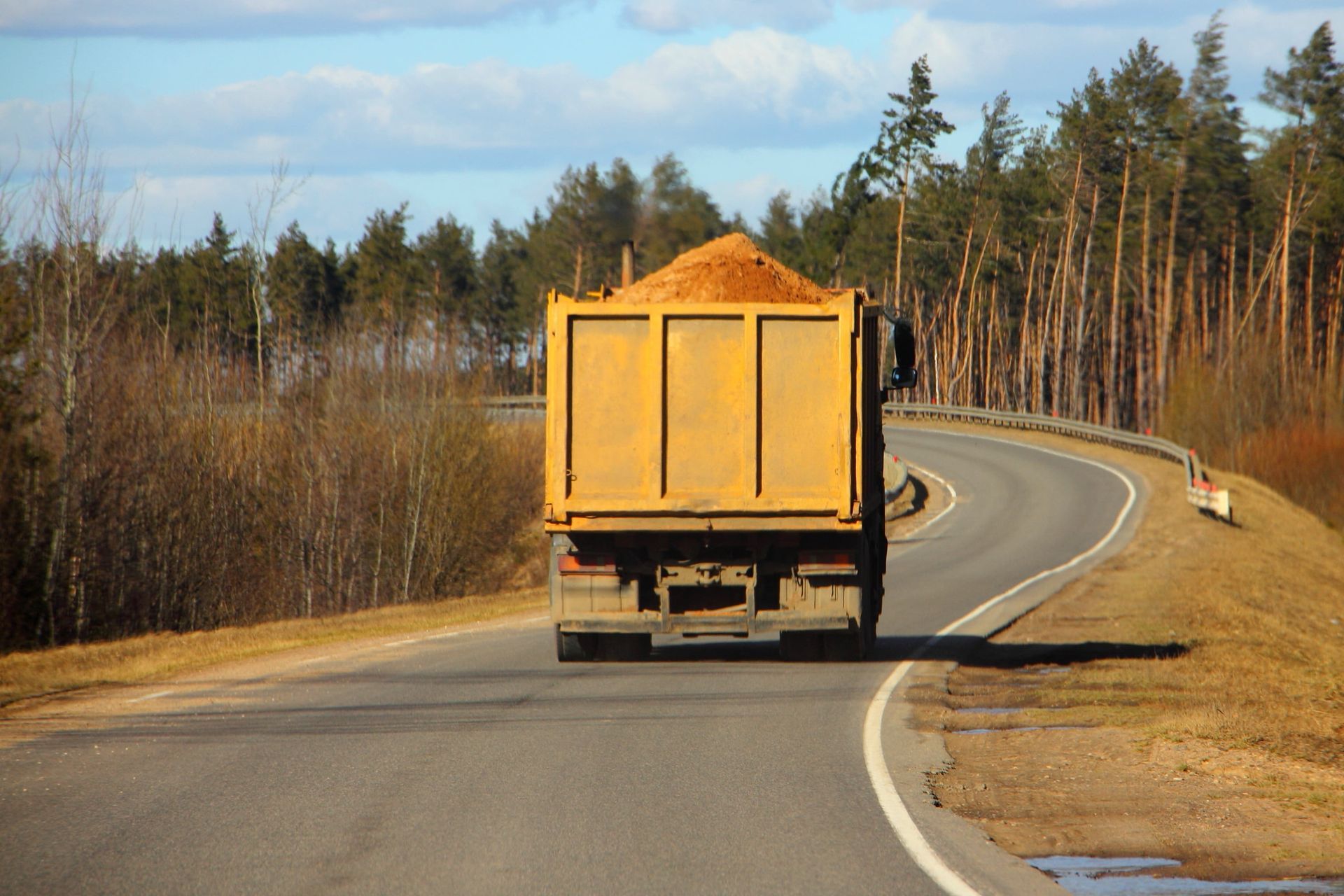 Orange truck driving along a winding rural road through trees and dry grass
