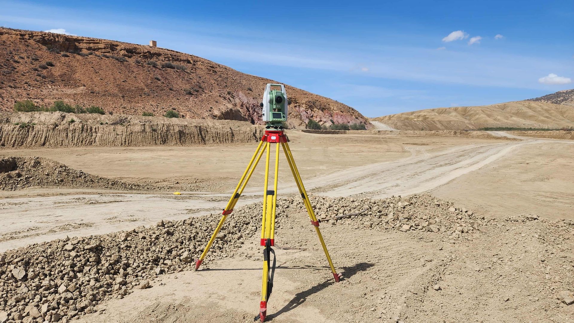 Surveying instrument on tripod in a dry rocky desert landscape under a clear blue sky