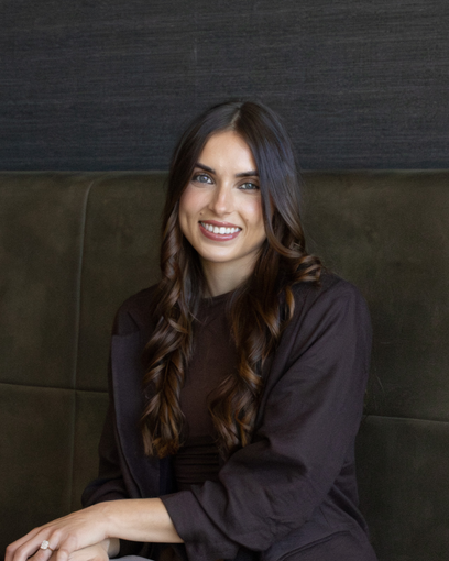 Smiling woman with long dark hair sitting on a dark green couch against a dark wall