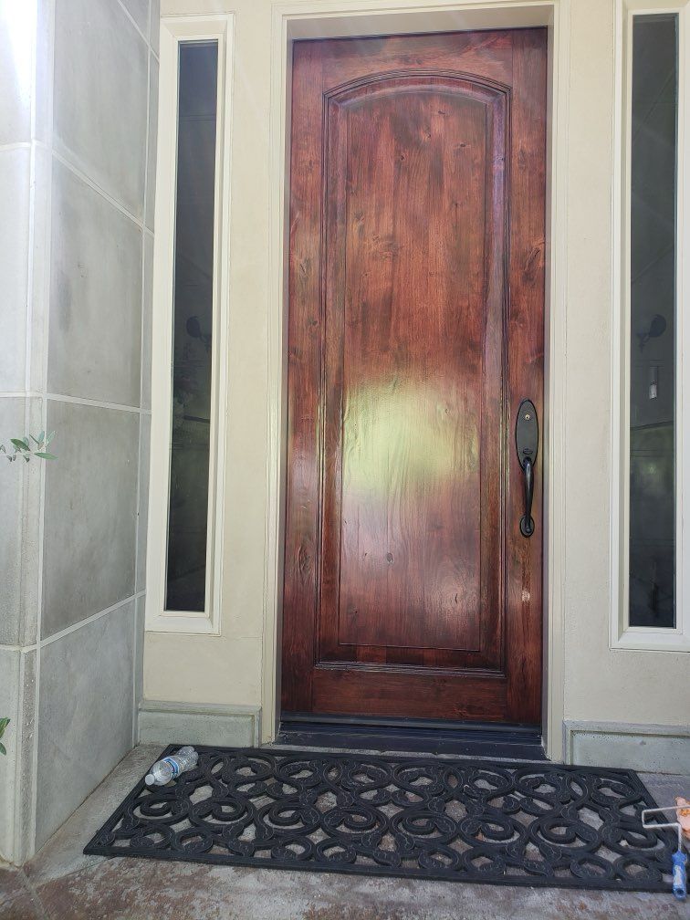 Wooden front door with sidelights, black doormat, and light-colored trim.