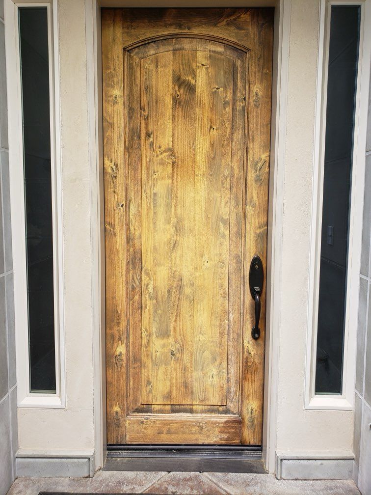 Wooden front door with sidelights. Stained yellow-brown with black hardware.