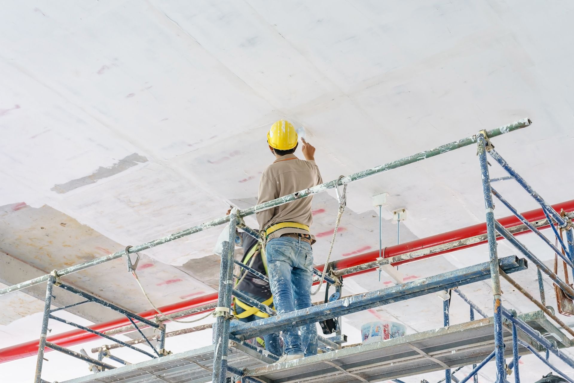 Construction worker on scaffolding, painting a white ceiling.
