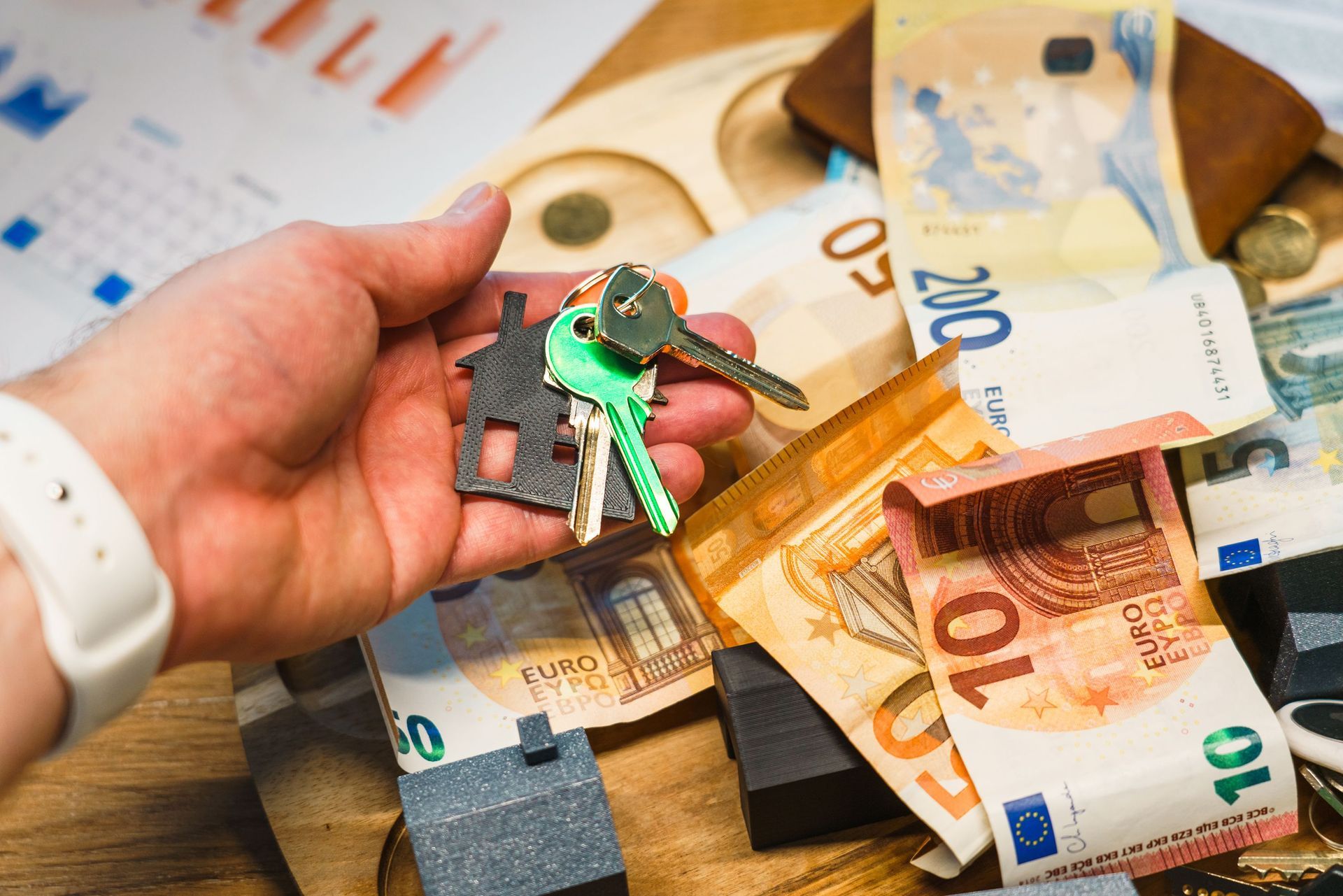 Hand die autosleutels vasthoudt boven eurobiljetten en een portemonnee op een tafel.
