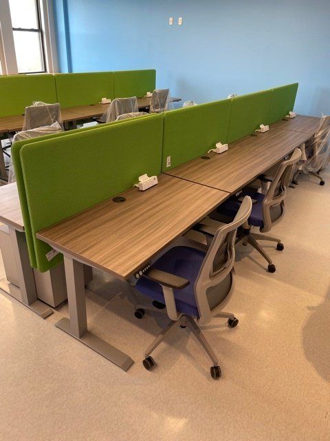 A row of desks with green dividers and chairs