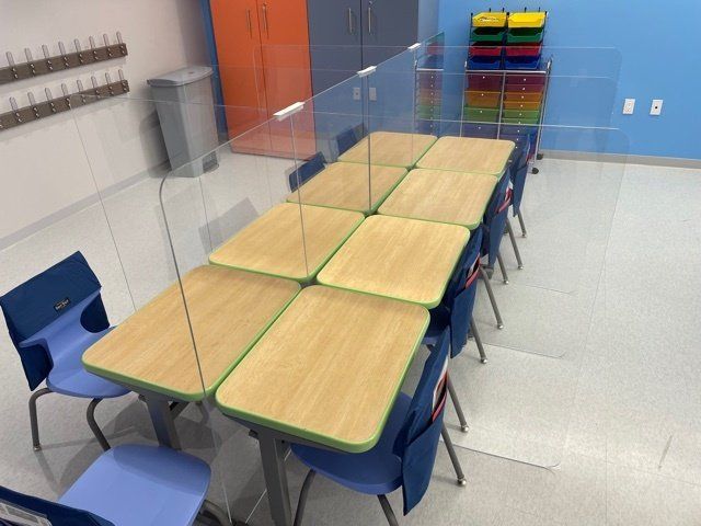 A classroom with tables and chairs and a clear divider